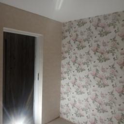 krzysztof gawor - Pokój po remoncie: ściana z tapetą w różowe róże, druga ściana pokryta jasnym tynkiem strukturalnym, widoczne ościeżnice drzwiowe.