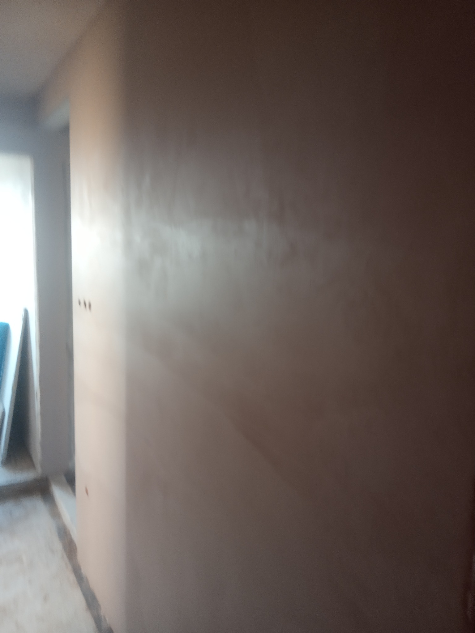 Świeżo nałożona, mokra gładź na ścianie w pomieszczeniu w trakcie remontu, widoczne ślady po narzędziach i nierównomierne wysychanie.
