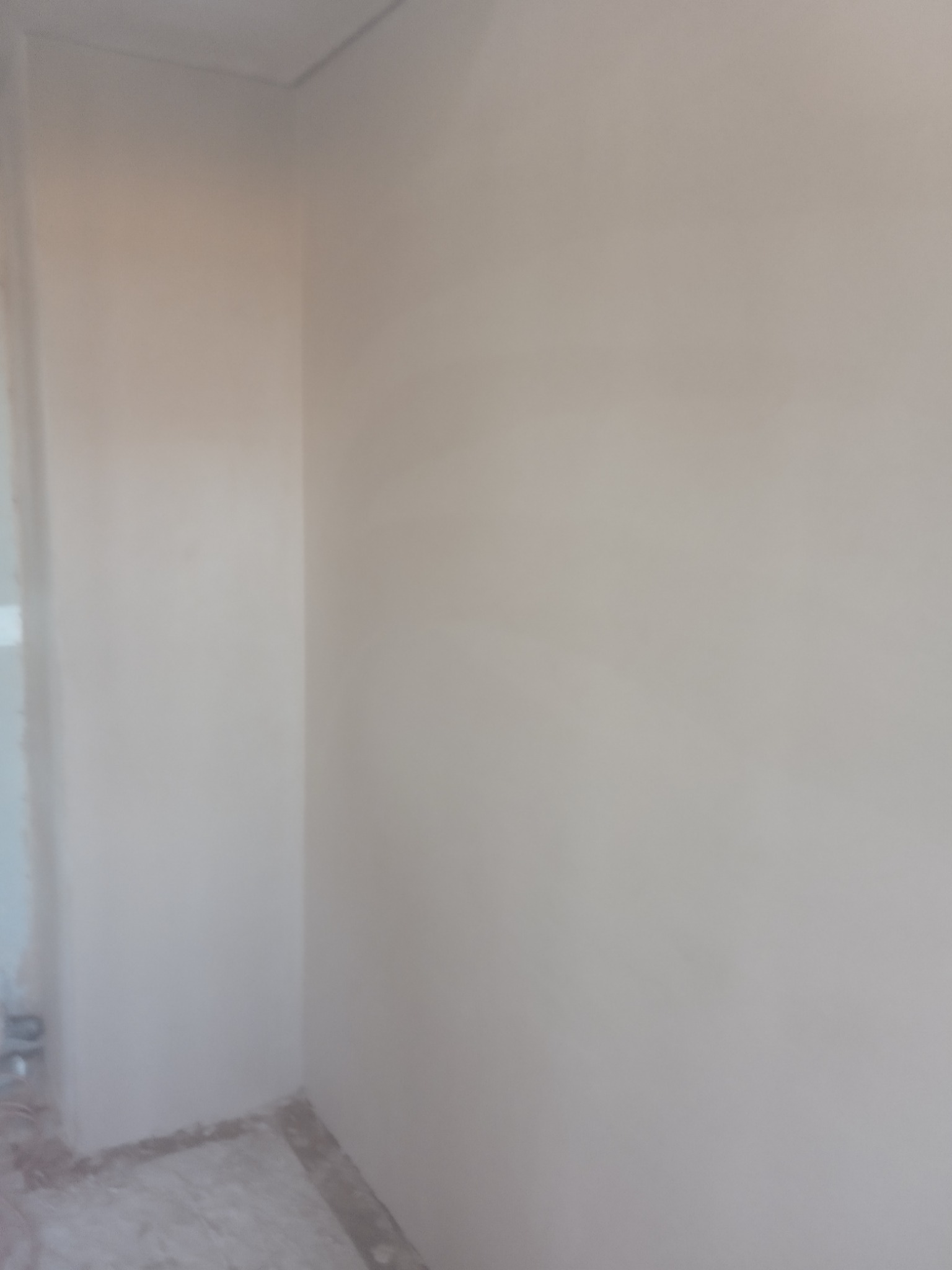 Świeżo wykończony róg pokoju z gładkimi, jasnymi ścianami i widocznymi śladami prac wykończeniowych na podłodze.