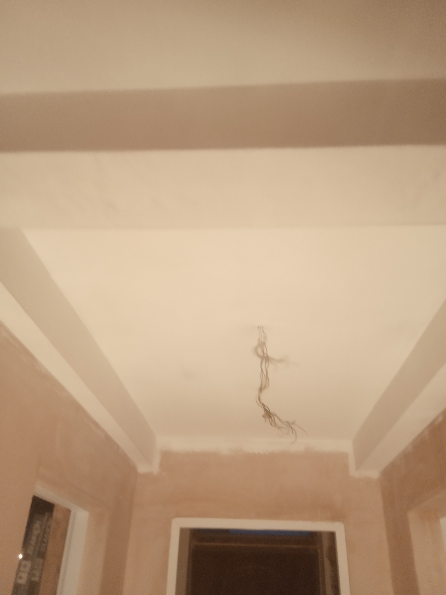 Wnętrze w trakcie wykańczania: sufit z listwami dekoracyjnymi i widocznymi przewodami elektrycznymi, ściany w stanie surowym przed malowaniem.