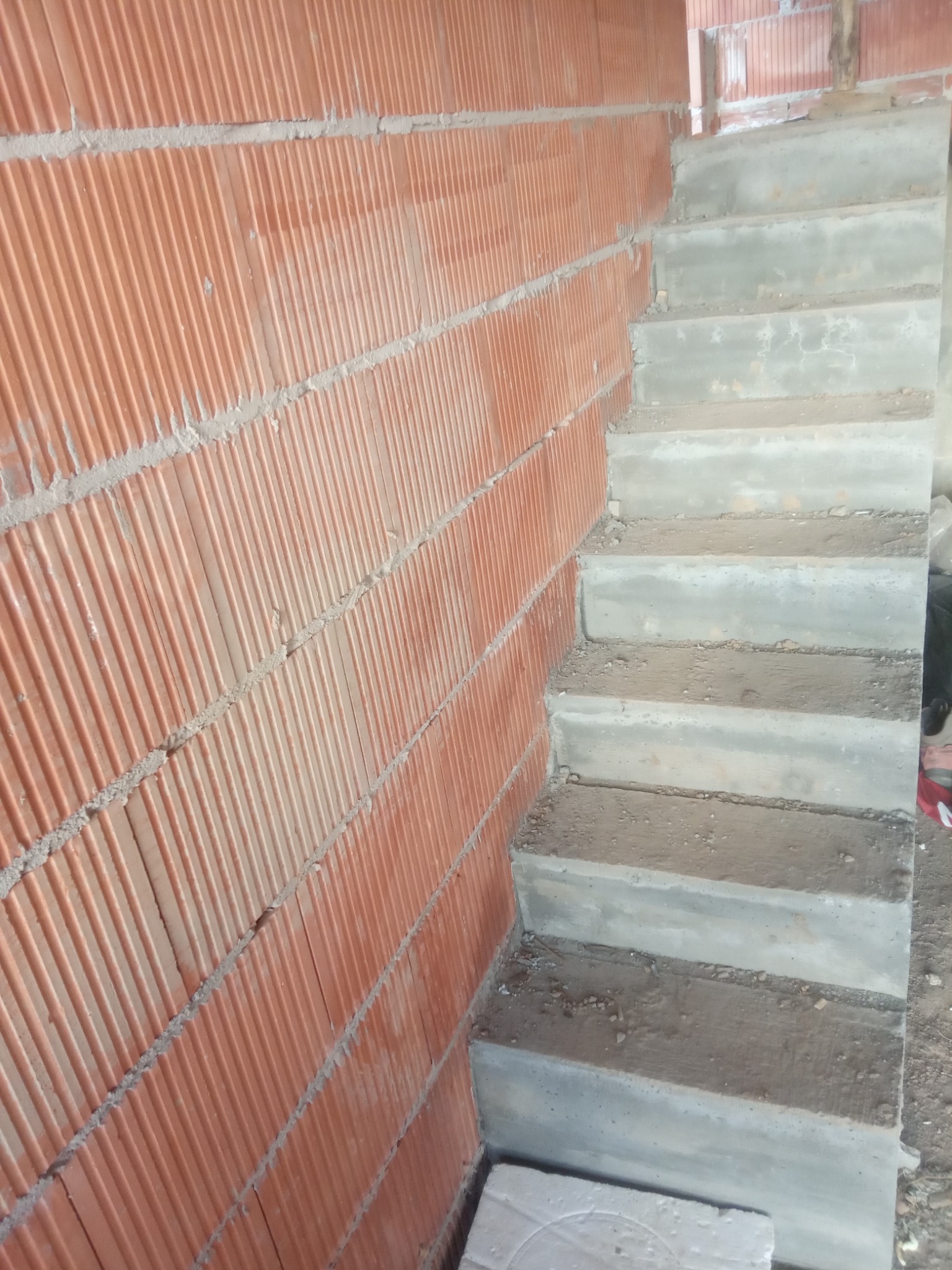 Surowe betonowe schody przylegające do ściany z czerwonej cegły dziurawki na etapie budowy.