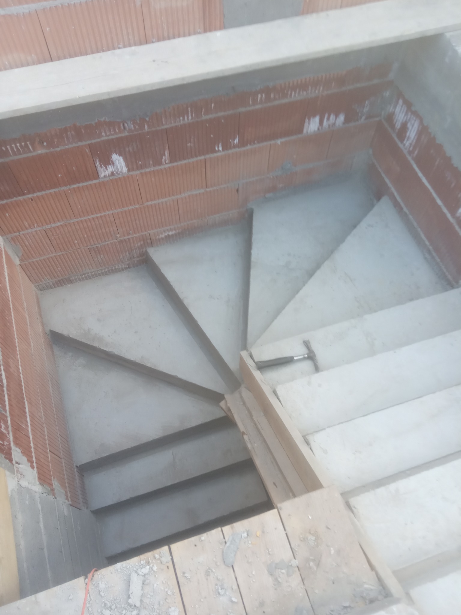 Betonowe schody w surowym stanie podczas budowy, widoczne ceglane ściany i młotek na jednym ze stopni.