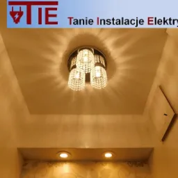 Kryształowy żyrandol sufitowy z trzema kulami w podwieszanym suficie, oświetlający łazienkę z dodatkowymi punktowymi lampami i panelem dostępowym do instalacji.