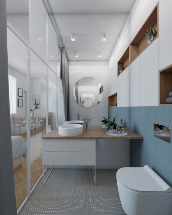 Nowoczesna łazienka z okrągłym lustrem, umywalką nablatową i błękitnymi płytkami, widok na sypialnię przez szklaną ścianę.