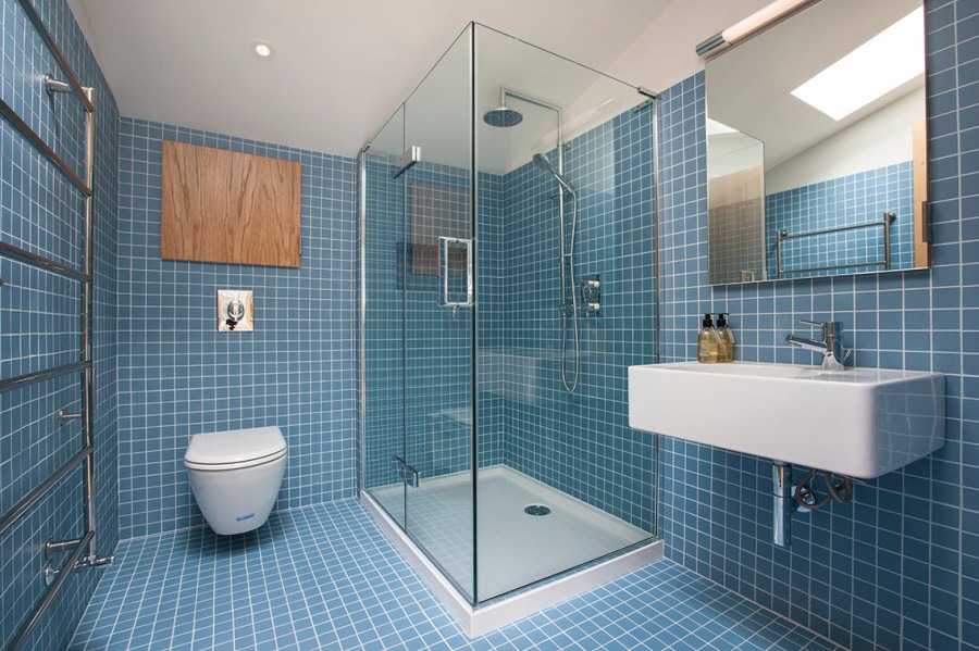 Niebieska łazienka z kwadratowymi płytkami, kabiną prysznicową ze szkła, wiszącą toaletą, grzejnikiem drabinkowym i prostokątną umywalką.