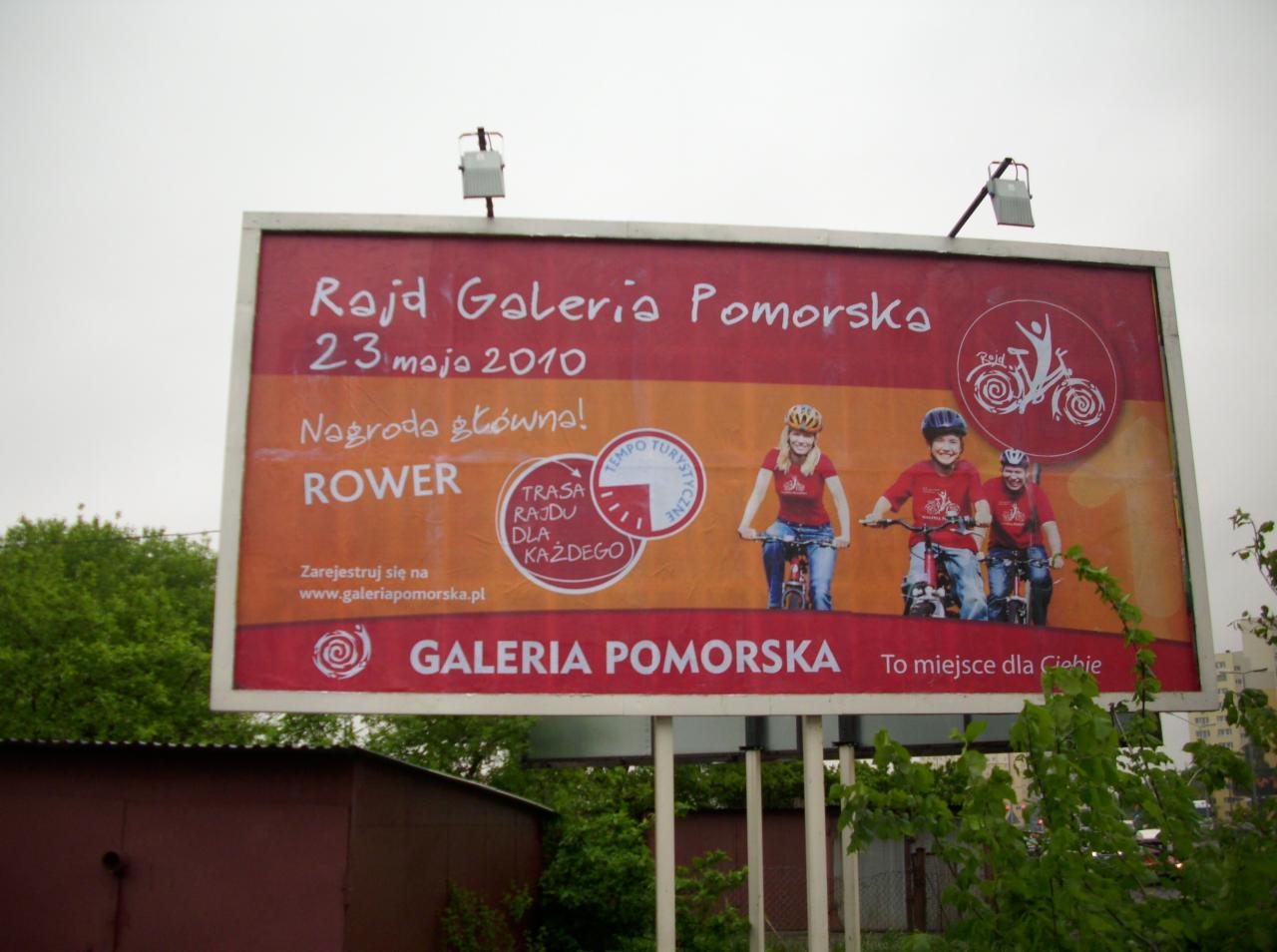Billboard reklamujący rajd rowerowy Galerii Pomorskiej, z wizerunkami uśmiechniętych dzieci na rowerach w kaskach i czerwonych koszulkach, informacją o nagrodzie głównej - rowerze oraz adresem...