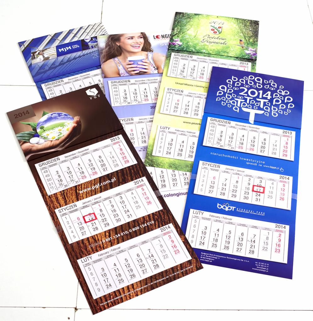Różne kalendarze ścienne z motywami firmowymi i układami miesięcznymi na rok 2013 i 2014, ułożone obok siebie.