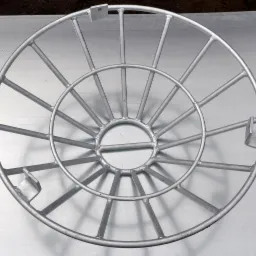 Metalowa konstrukcja z okrągłymi obręczami i wspornikami, prawdopodobnie element rusztowania lub zabezpieczenia, spawana, pomalowana na szaro, widoczne ślady po spawaniu.