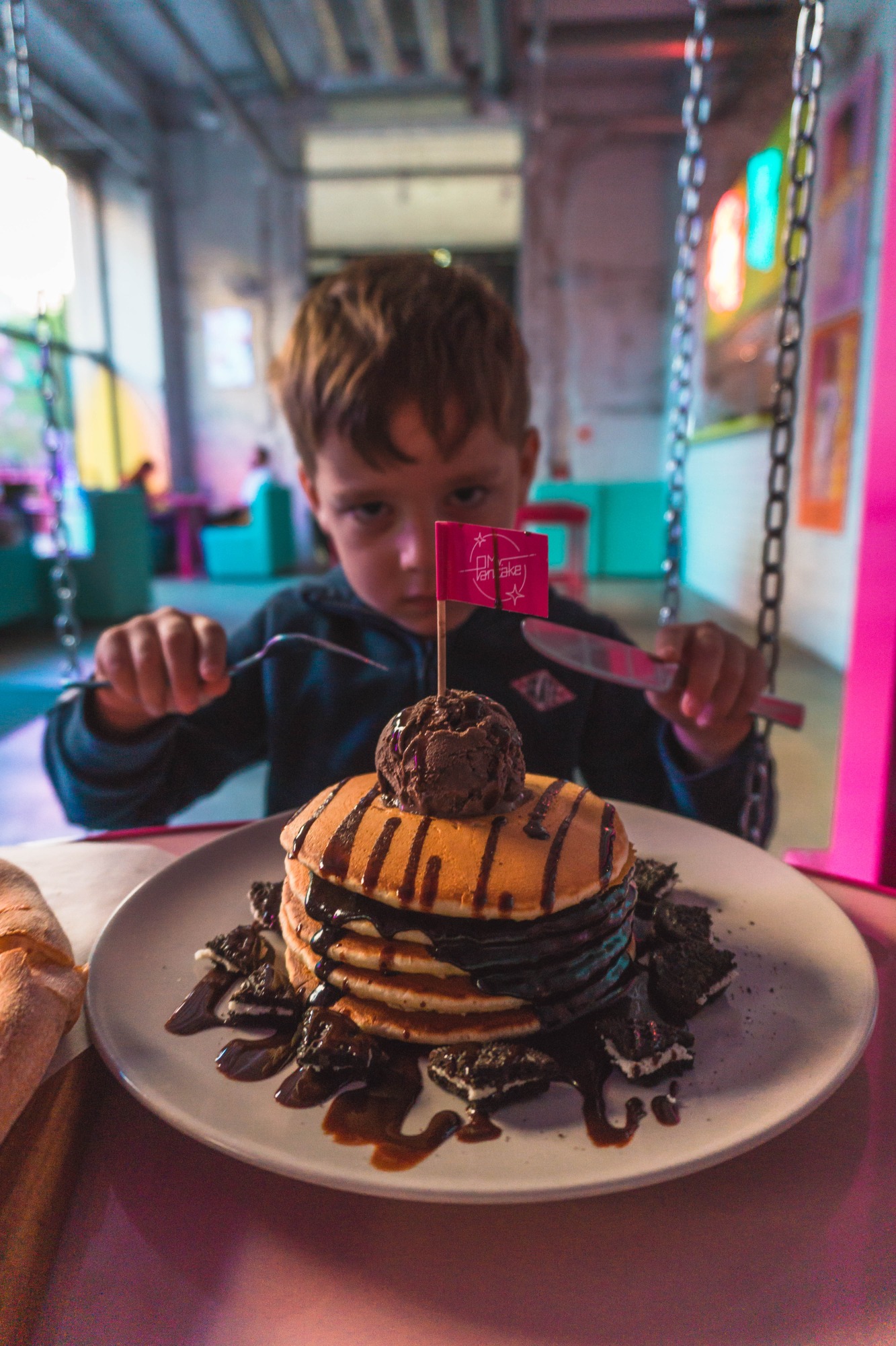 Chłopiec w restauracji w Warszawie przygotowuje się do jedzenia wieży z naleśników z lodami i polewą czekoladową, udekorowanej flagą.