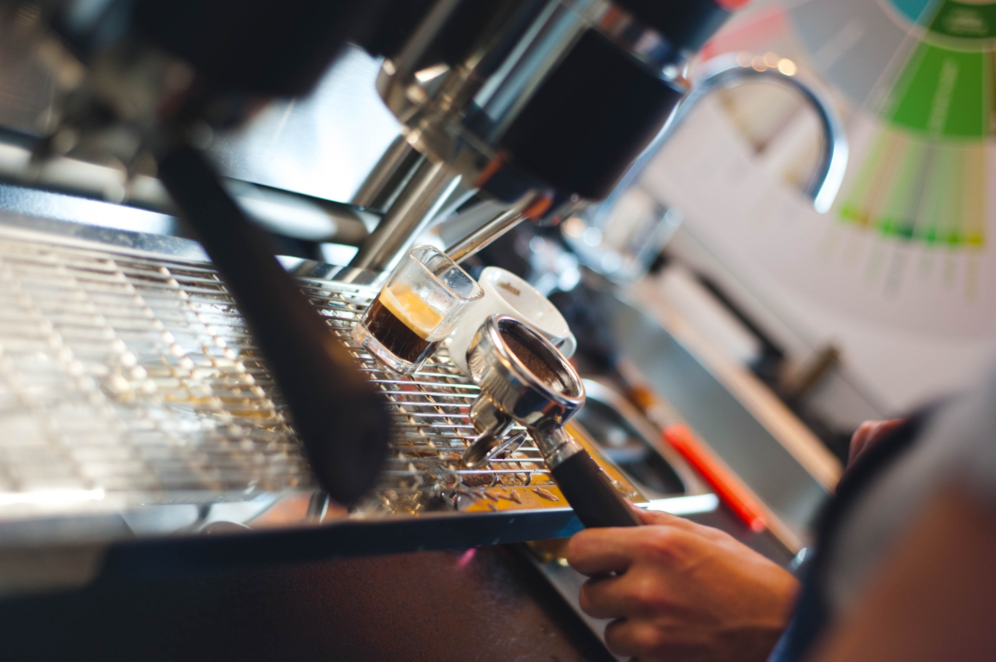 Ekspres do kawy: proces parzenia espresso w szklanym kieliszku, uchwyt z kawą w dłoni, krople kawy na metalowej kratce.