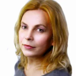 Portret kobiety o jasnych włosach i przenikliwym spojrzeniu, ujęcie z dołu, na białym tle. Subtelny makijaż i delikatny uśmiech.