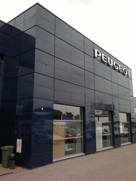 Elewacja budynku salonu samochodowego Peugeot w Rybniku, wykończona ciemnymi płytami warstwowymi, z widocznym logo Peugeot na górze fasady.