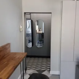 Wnętrze mieszkania po remoncie: szare ściany, drewniany blat, designerski stołek barowy na tle wzorzystej posadzki i lustra w korytarzu.