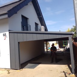 MARL - Nowoczesny dom jednorodzinny z dobudowanym zadaszeniem garażowym w kolorze grafitowym, widoczny pracownik w ubraniu roboczym, narzędzia budowlane w tle.