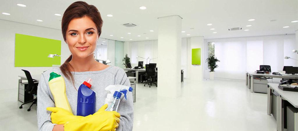 Uśmiechnięta kobieta w żółtych rękawicach trzymająca środki czystości w nowoczesnym, jasnym biurze z białymi podłogami i zielonymi akcentami.