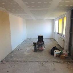Drapinski Piotr Drapinski Usługi Ogólnobudowlane - Pokój w trakcie remontu: zamontowane płyty kartonowo-gipsowe na suficie z widocznymi punktami szpachlowania, ściany przygotowane do malowania, na podłodze narzędzia i odkurzacz przemysłowy.