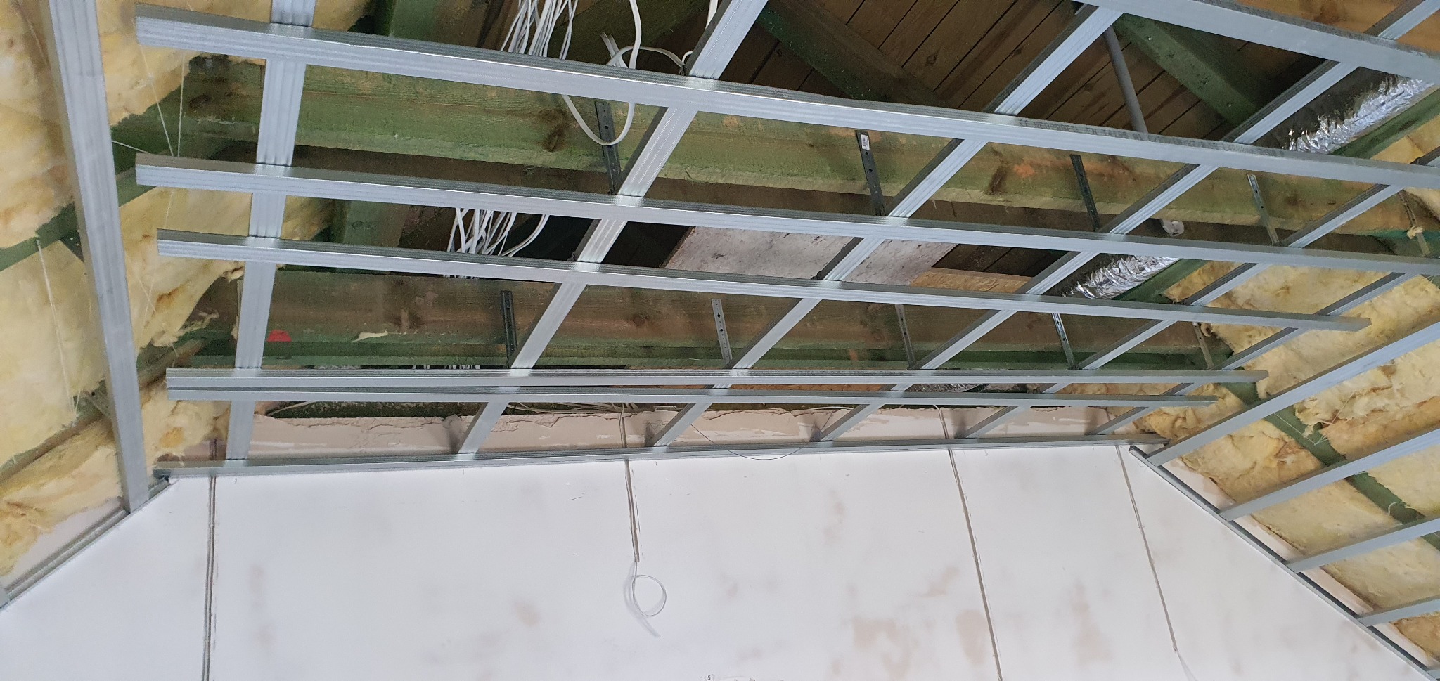 Sufit podwieszany z metalową konstrukcją, częściowo obłożony płytami kartonowo-gipsowymi, widoczne ocieplenie z wełny mineralnej i instalacja elektryczna.