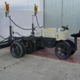 Samobieżne urządzenie do wylewania posadzek z laserowym systemem poziomowania, widoczne koła i siedzenie operatora na tle budynku.