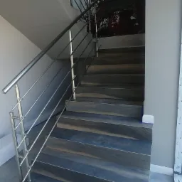 Schody wyłożone płytkami imitującymi drewno z balustradą ze stali nierdzewnej, widok z dołu, w tle ściana z dekoracyjną tapetą.