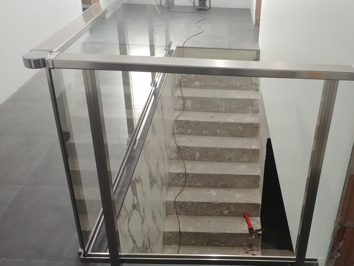 Montaż balustrady szklanej ze stali nierdzewnej w Świebodzinie, widok z góry na betonowe schody z częściowo wykończonymi ścianami, widoczny pistolet do kleju.