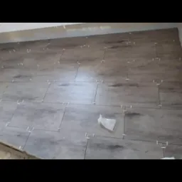 Ułożone płytki podłogowe imitujące drewno z użyciem krzyżyków dystansowych, widoczny fragment ściany i folia ochronna.