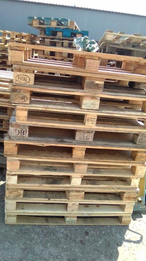 Stos palet EPAL z widocznymi oznaczeniami producenta i datami produkcji na tle hali magazynowej.