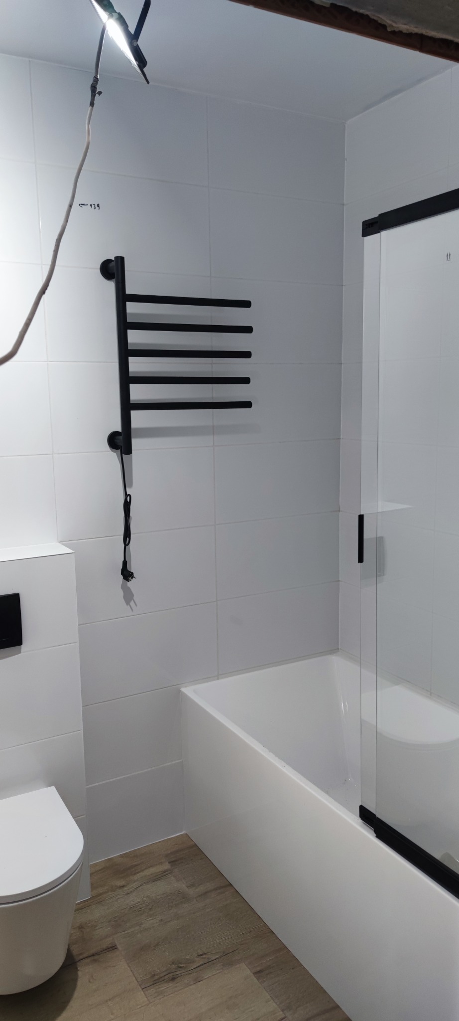 Biała łazienka po remoncie w Kampinosie: kabina prysznicowa, grzejnik drabinkowy, toaleta. Minimalistyczny design, płytki w jasnym odcieniu, drewnopodobna podłoga.