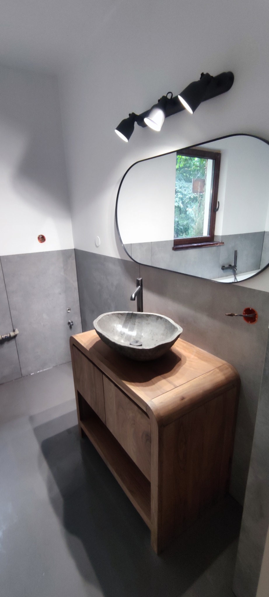 Nowoczesna łazienka w Kampinos: drewniana szafka z kamienną umywalką, szare płytki, podłużne lustro i oświetlenie punktowe. Minimalistyczny design.