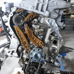 Odkryty silnik BMW N47 z widocznym łańcuchem rozrządu i napinaczami, umieszczony na palecie w warsztacie.