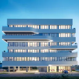 Nowoczesny budynek biurowy z podświetlanymi balkonami i przeszklonymi fasadami, widoczny tramwaj w tle.