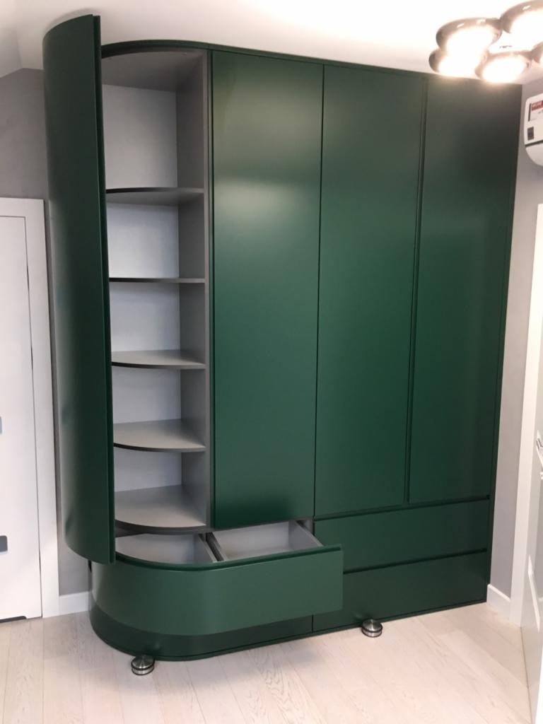 Zielona szafa z zaokrąglonym narożnikiem i otwartą szufladą, widoczne półki wewnątrz, minimalistyczny design.
