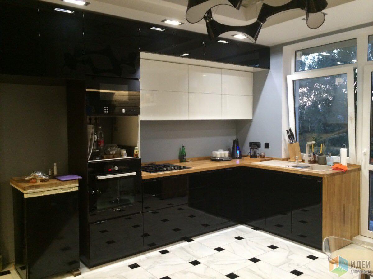 Czarno-biała kuchnia z drewnianym blatem i marmurową podłogą w szachownicę, widok na okno z zielenią na zewnątrz, nowoczesne oświetlenie sufitowe.