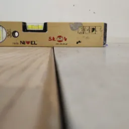 Poziomica na styku ułożonych paneli podłogowych i płytek ceramicznych, widoczne drobne zabrudzenia na płytkach.