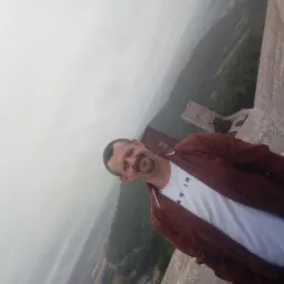 Mężczyzna w brązowej kurtce pozuje na tle zamku i mglistego krajobrazu. Nietypowa perspektywa z góry.