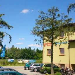 Budynek firmy Termo-Project z logiem na elewacji, zaparkowane samochody i motocykle, widoczne banery reklamowe i drzewa w słoneczny dzień.