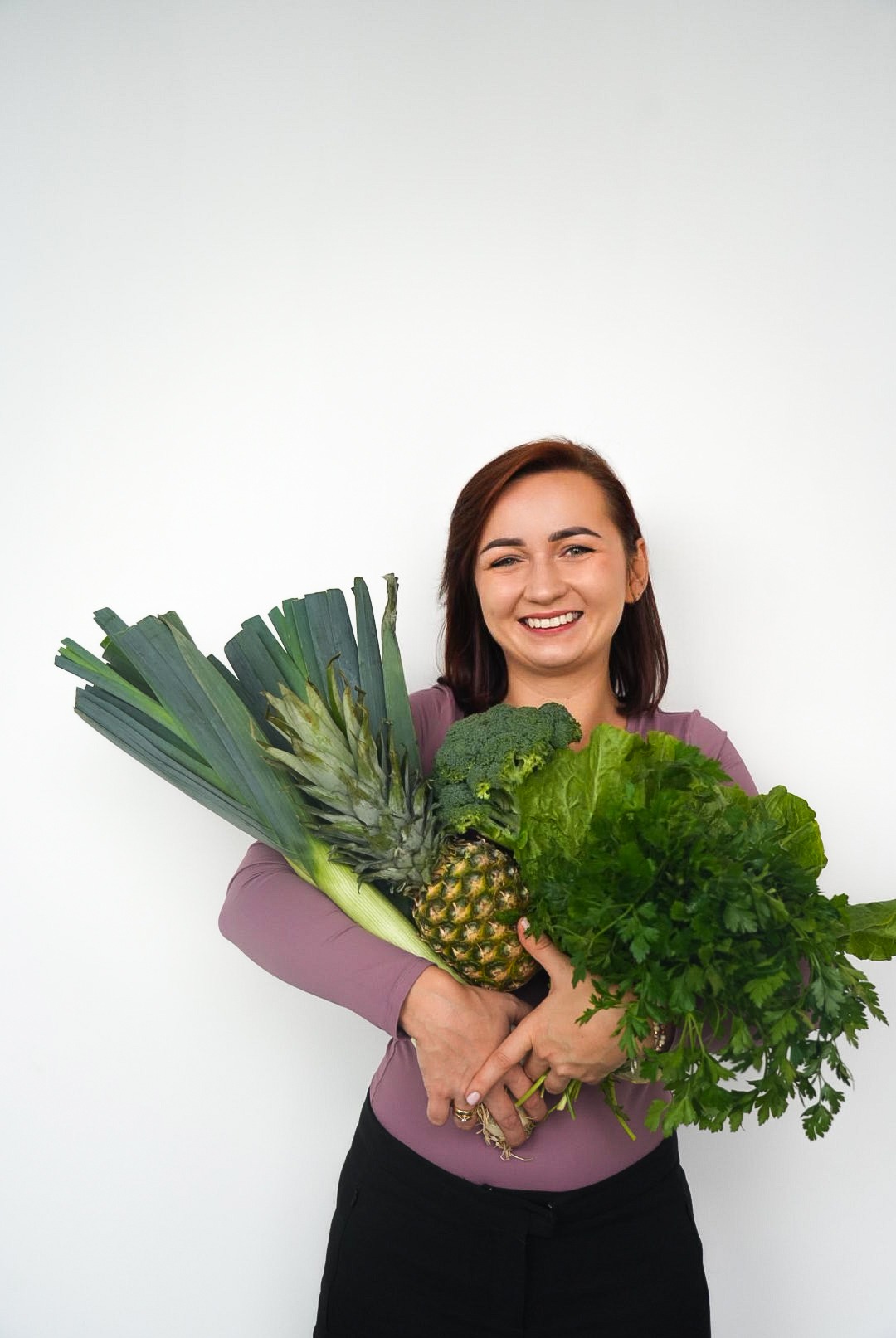 Uśmiechnięta kobieta trzymająca bukiet świeżych warzyw i owoców: por, ananas, brokuły i zielenina. Zdrowe odżywianie i porady żywieniowe.