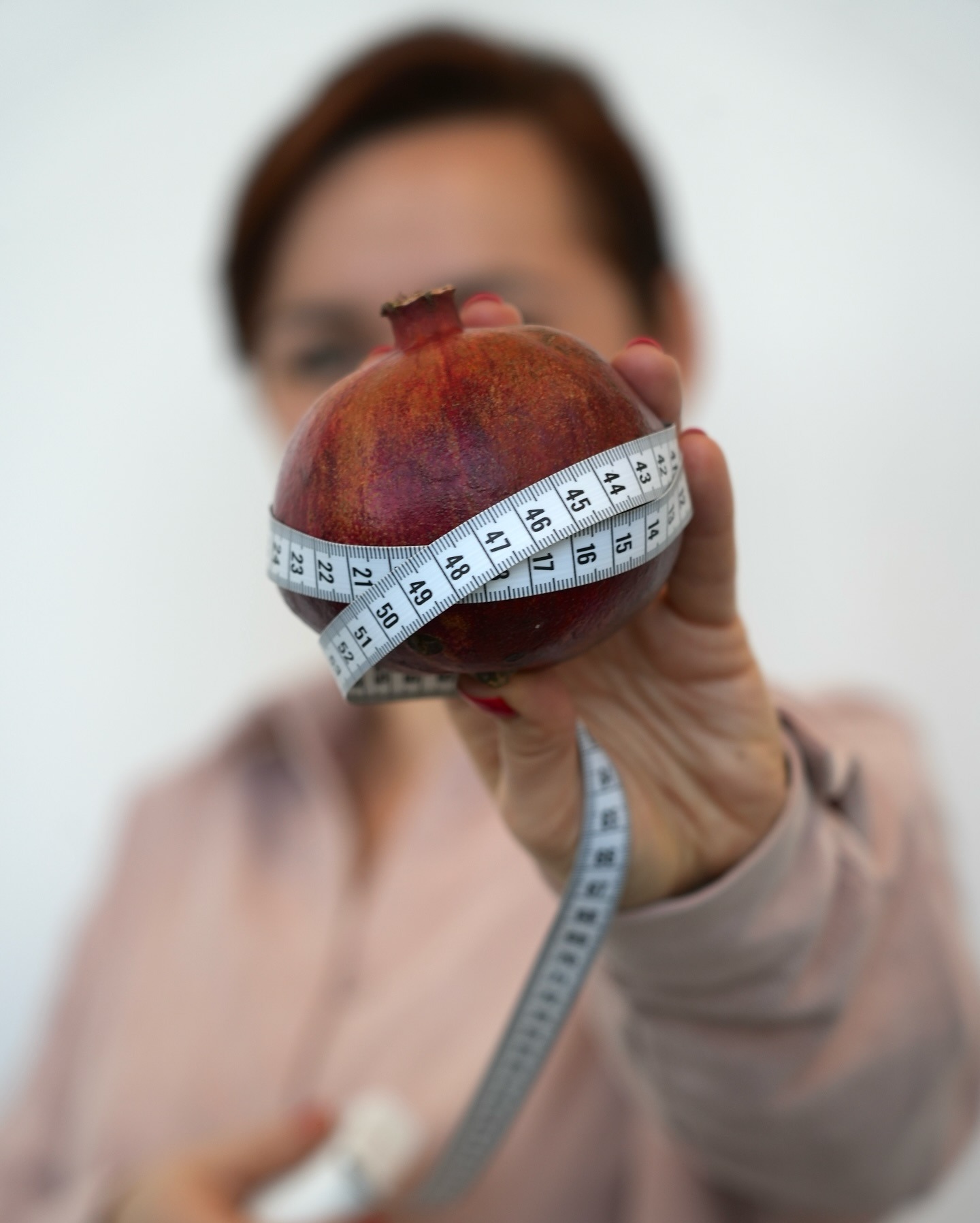 Kobieta prezentuje granat owinięty miarką krawiecką, symbolizujący zdrowe odżywianie i kontrolę wagi. Ujęcie z bliska, miękkie światło.