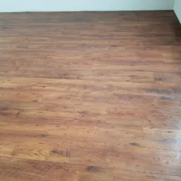 Ułożona podłoga z paneli imitujących ciemne drewno, widok z góry, jasne ściany w tle.