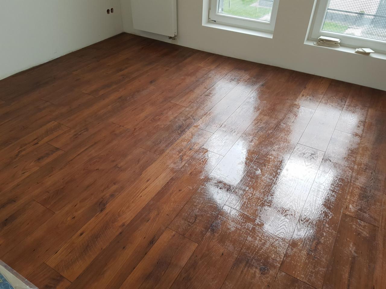 Nowo ułożona, lakierowana podłoga z paneli imitujących drewno w jasnym pokoju z dwoma oknami. Widoczne refleksy światła na powierzchni podłogi.