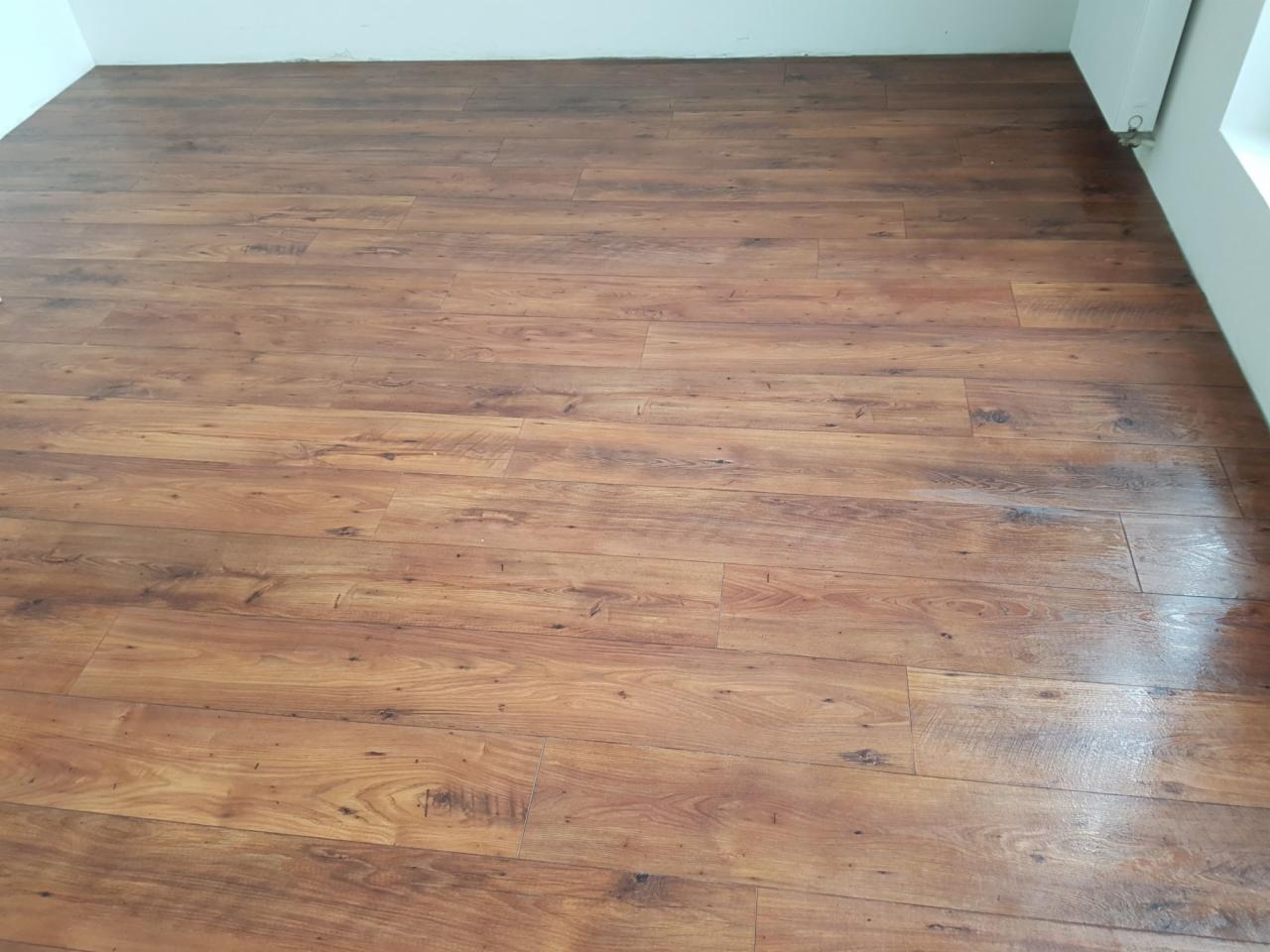 Ułożona podłoga z paneli imitujących ciemne drewno, widok z góry, jasne ściany w tle.