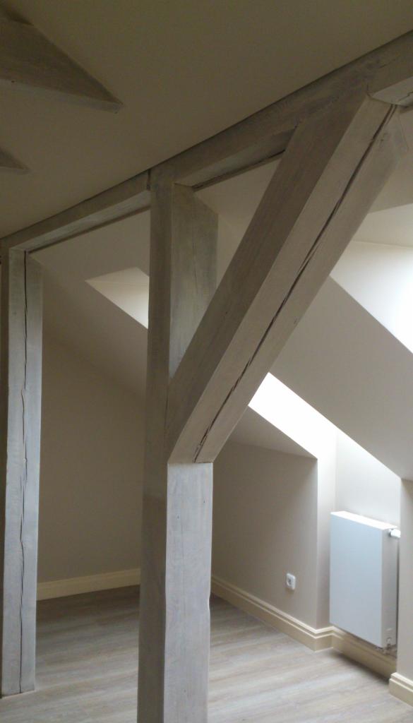 Drewniane belki konstrukcyjne w odnowionym poddaszu z widocznym oknem dachowym i grzejnikiem.