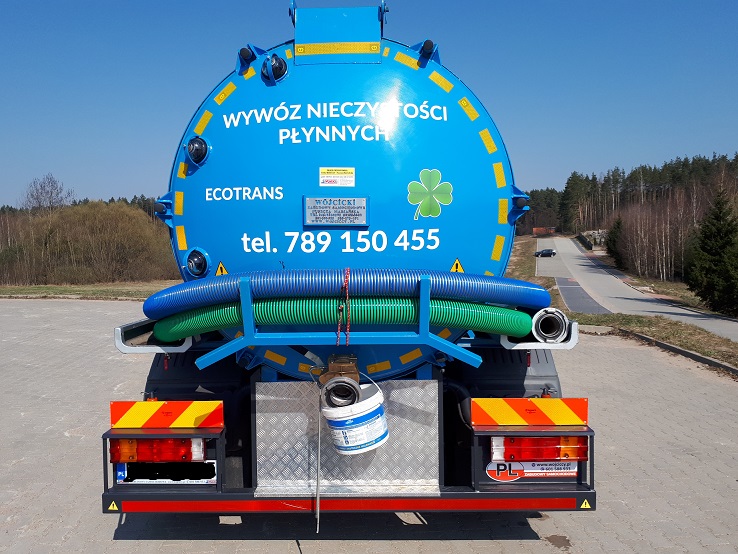 Niebieska cysterna asenizacyjna z napisem 'Wywóz nieczystości płynnych' i logiem firmy Ecotrans, widok z tyłu, z widocznymi wężami i tablicą rejestracyjną.