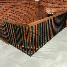 Nowoczesna balustrada schodowa z czarnymi metalowymi słupkami i drewnianą poręczą, widoczna na tle ściany z czerwonej cegły.