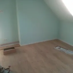 Poddasze z drewnopodobną podłogą w trakcie układania, widoczna paczka paneli 'Clic Rigid Core Designbe' oraz piła ukośnica.