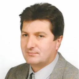 Portret mężczyzny w szarej marynarce i białej koszuli na jasnym tle.