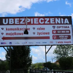 Billboard reklamujący różne rodzaje ubezpieczeń, w tle budynki i drzewa.