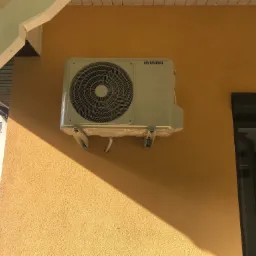 Zamontowana jednostka zewnętrzna klimatyzatora Hyundai na żółtej ścianie budynku, widoczne przewody i cień.