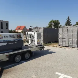 Piaskowanie kontenerów transportowych z użyciem mobilnej piaskarki SodaBlast SB-500 Trailer, operator w kombinezonie ochronnym na dachu kontenera, widoczne ślady piaskowania.