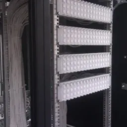 Panel krosowniczy z ułożonymi kablami telekomunikacyjnymi w szafie rack, widoczne oznaczenia numeracji kabli.