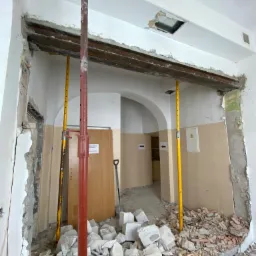 Demontaż ściany w Chorzowie, widoczne gruz, podpory pionowe i odsłonięta konstrukcja stropu z metalowym profilem.